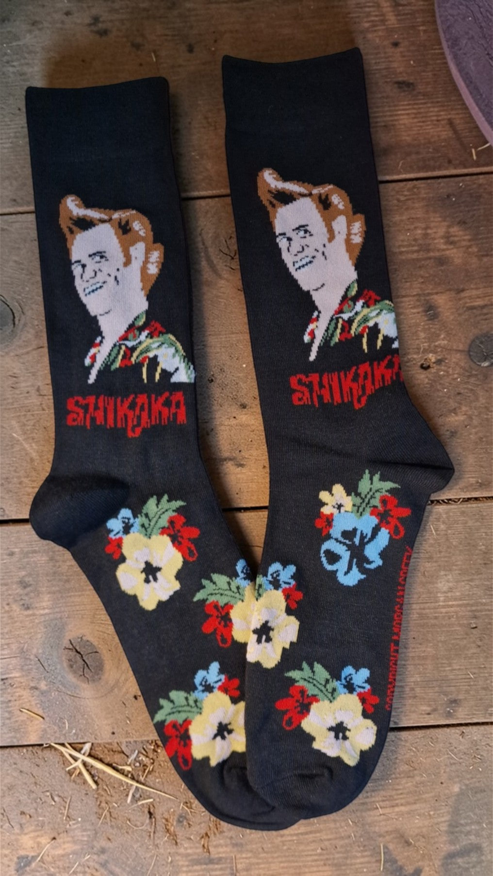 Black socks with embroidered design and 'Saukaki' text on a wooden surface