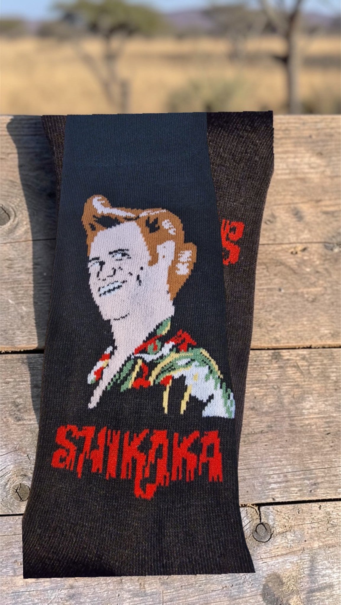 Sock with a graphic design of a person with red hair and 'Shikaka' text on a wooden surface.