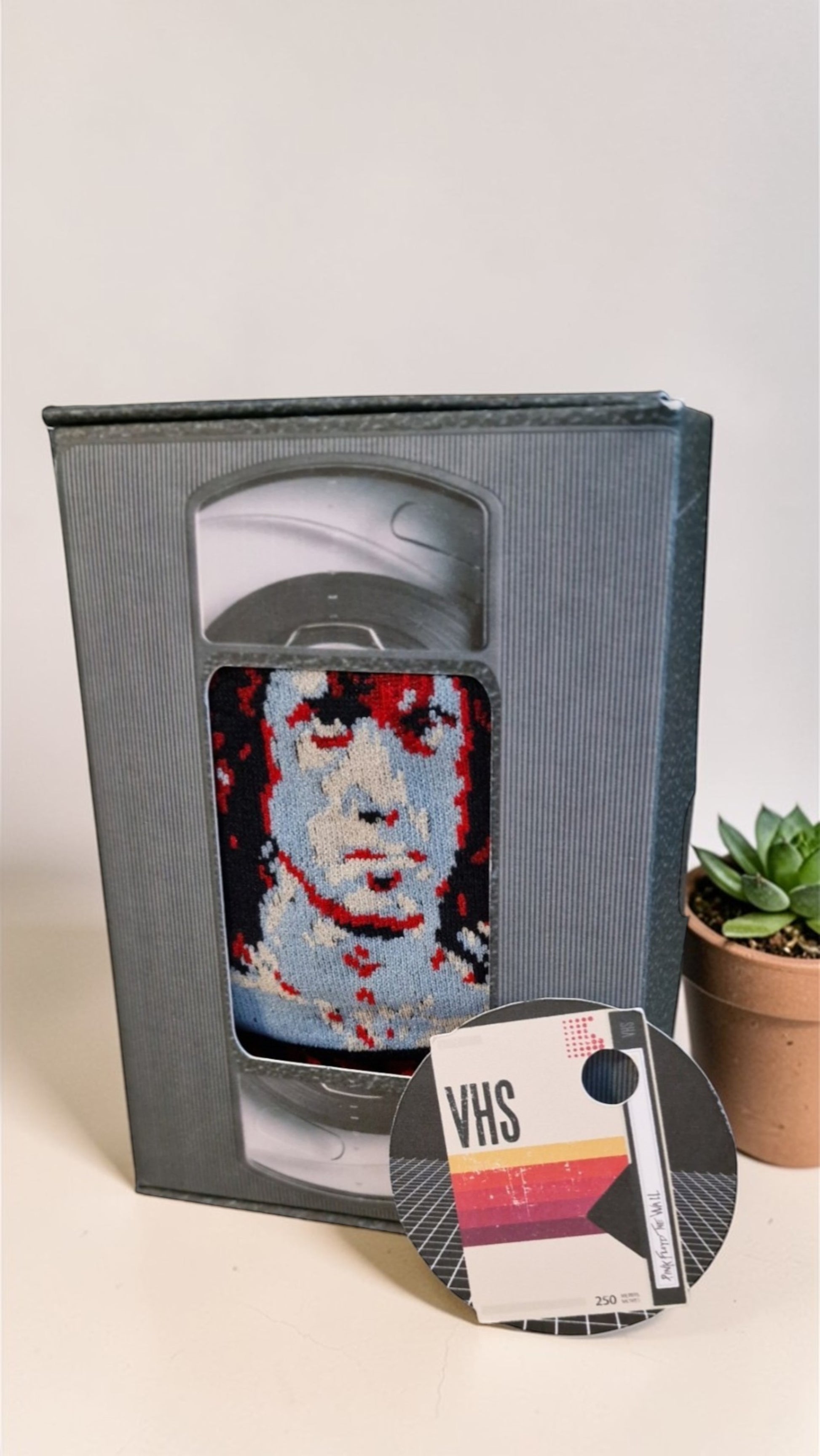 VHS tape with a face design and a small potted plant on a light background