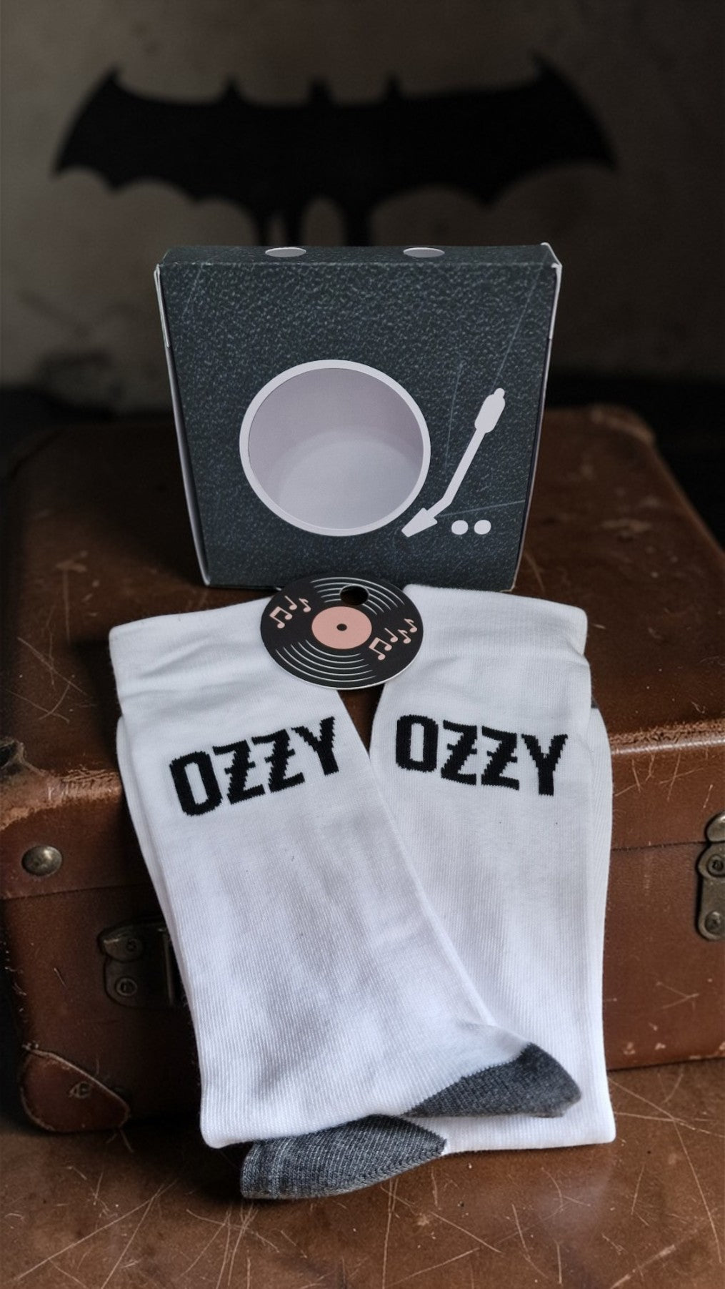 White socks with 'Ozzy' text on a brown surface with a record and packaging in the background.