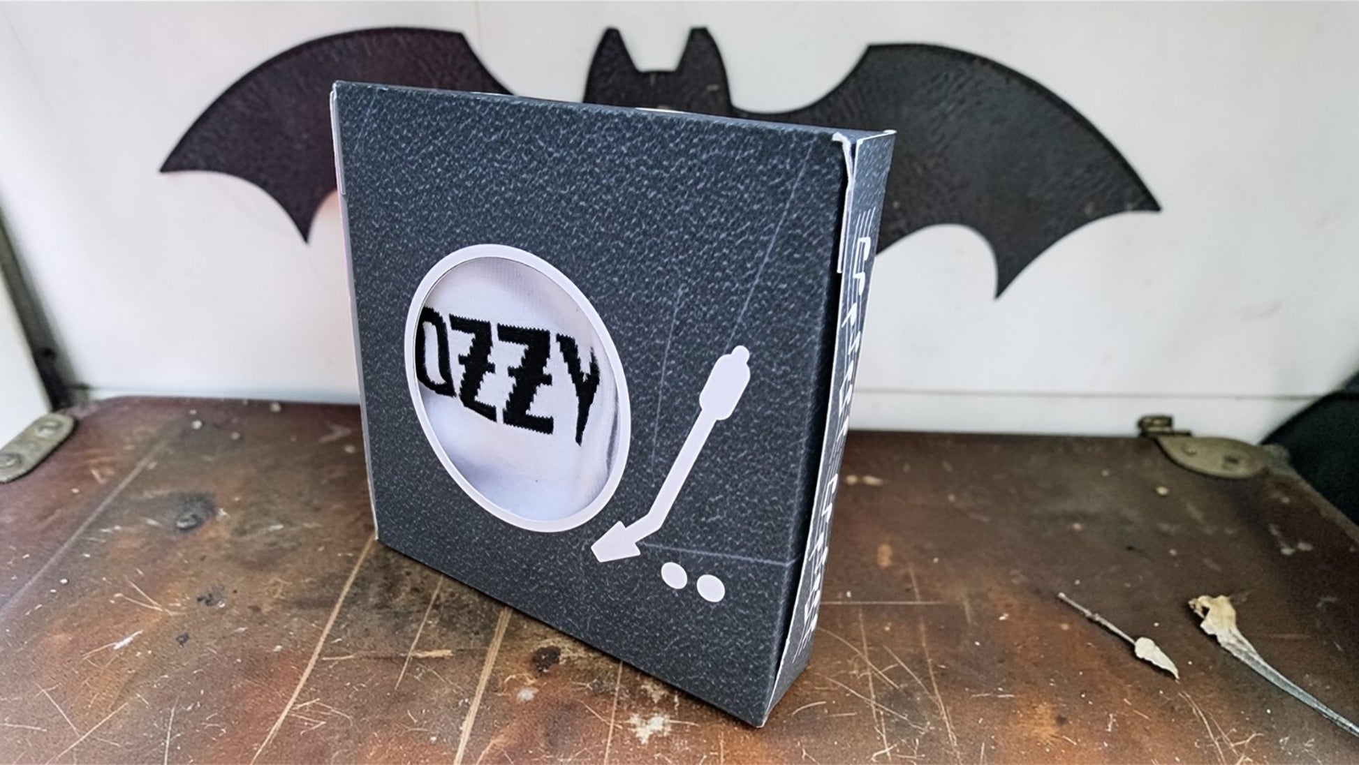 Ozzy Osbourne album cover on a wooden surface with a bat symbol in the background