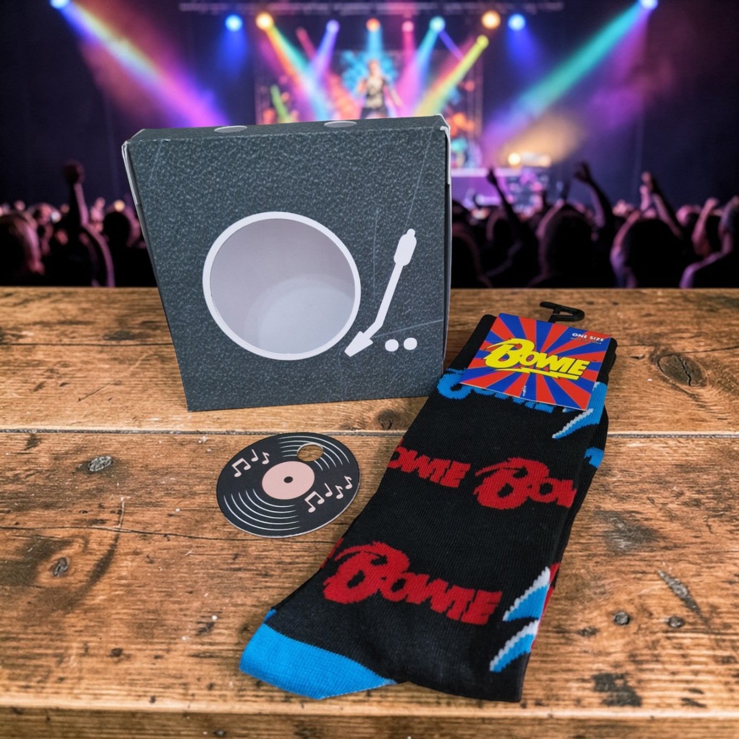 Black socks with red 'Bowie' text on a wooden surface, with a concert backdrop.