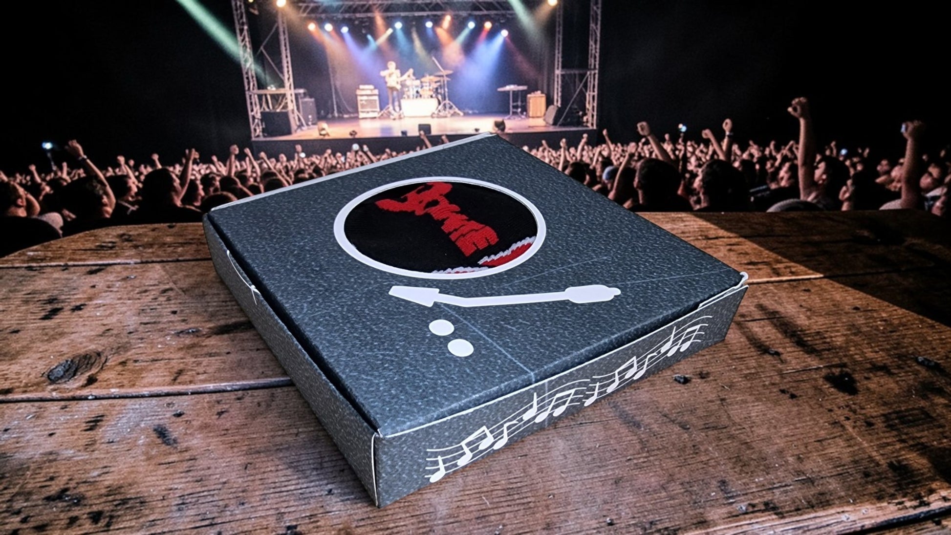 Cardboard box with a logo on a wooden surface in front of a concert stage.