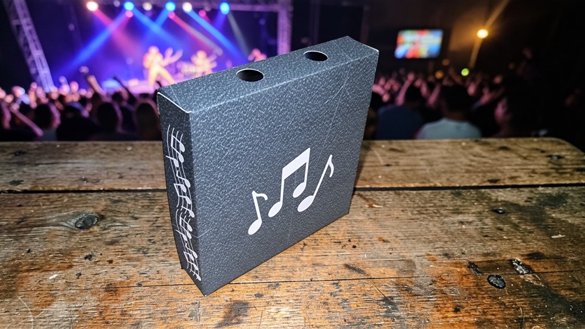 Black box with music notes on a wooden surface, concert lights in the background