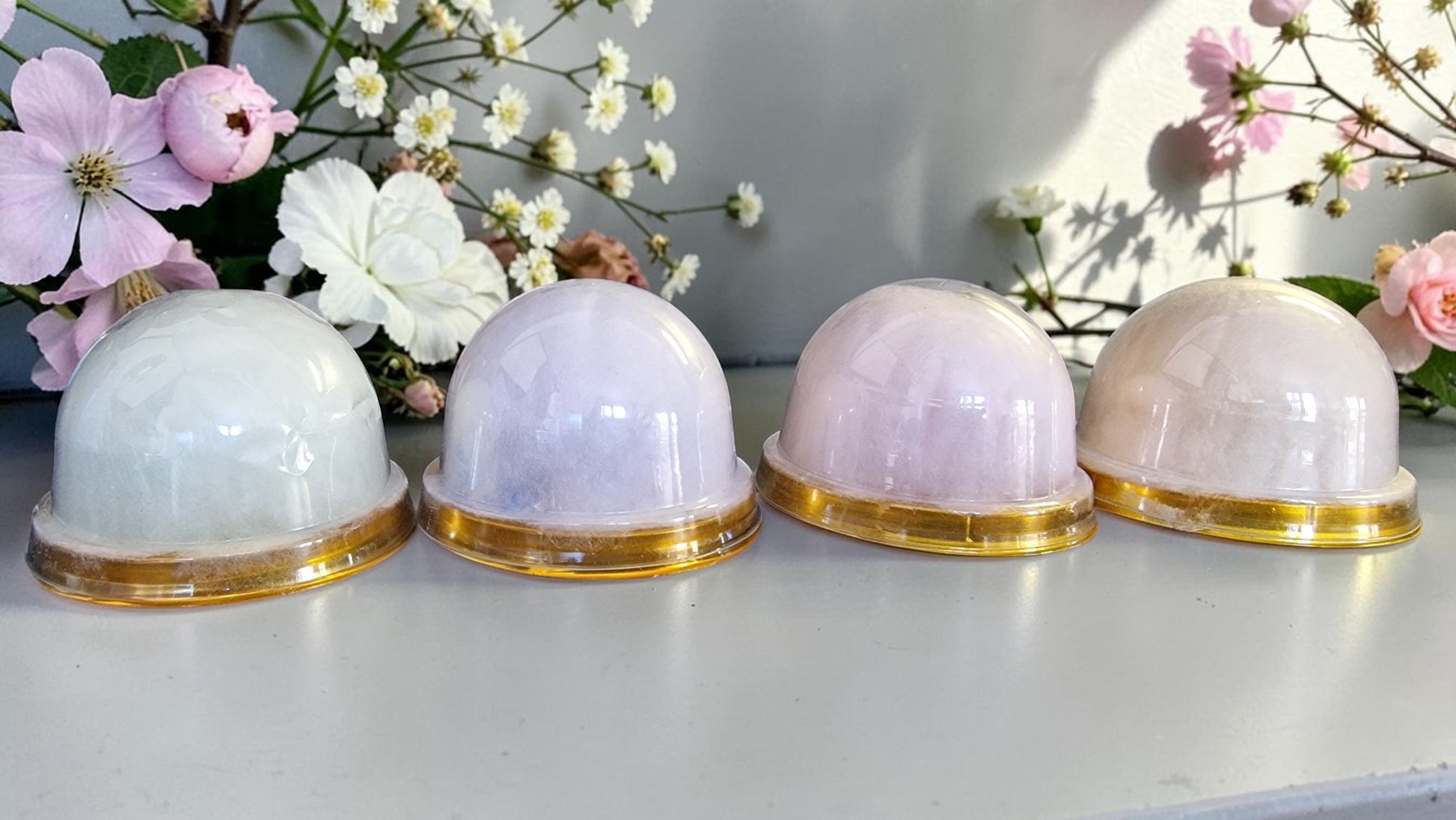 Four spherical containers with gold bases on a light surface with flowers in the background