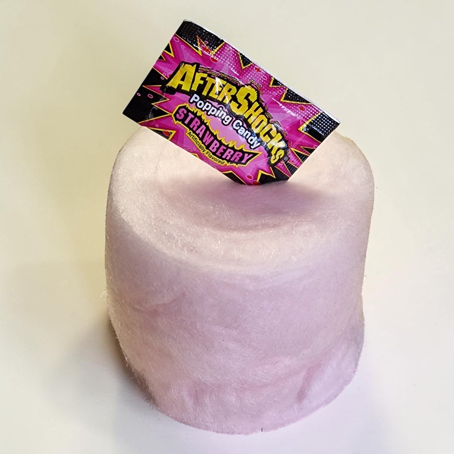 Pink cotton candy with a 'Aftershock' candy package on top against a white background