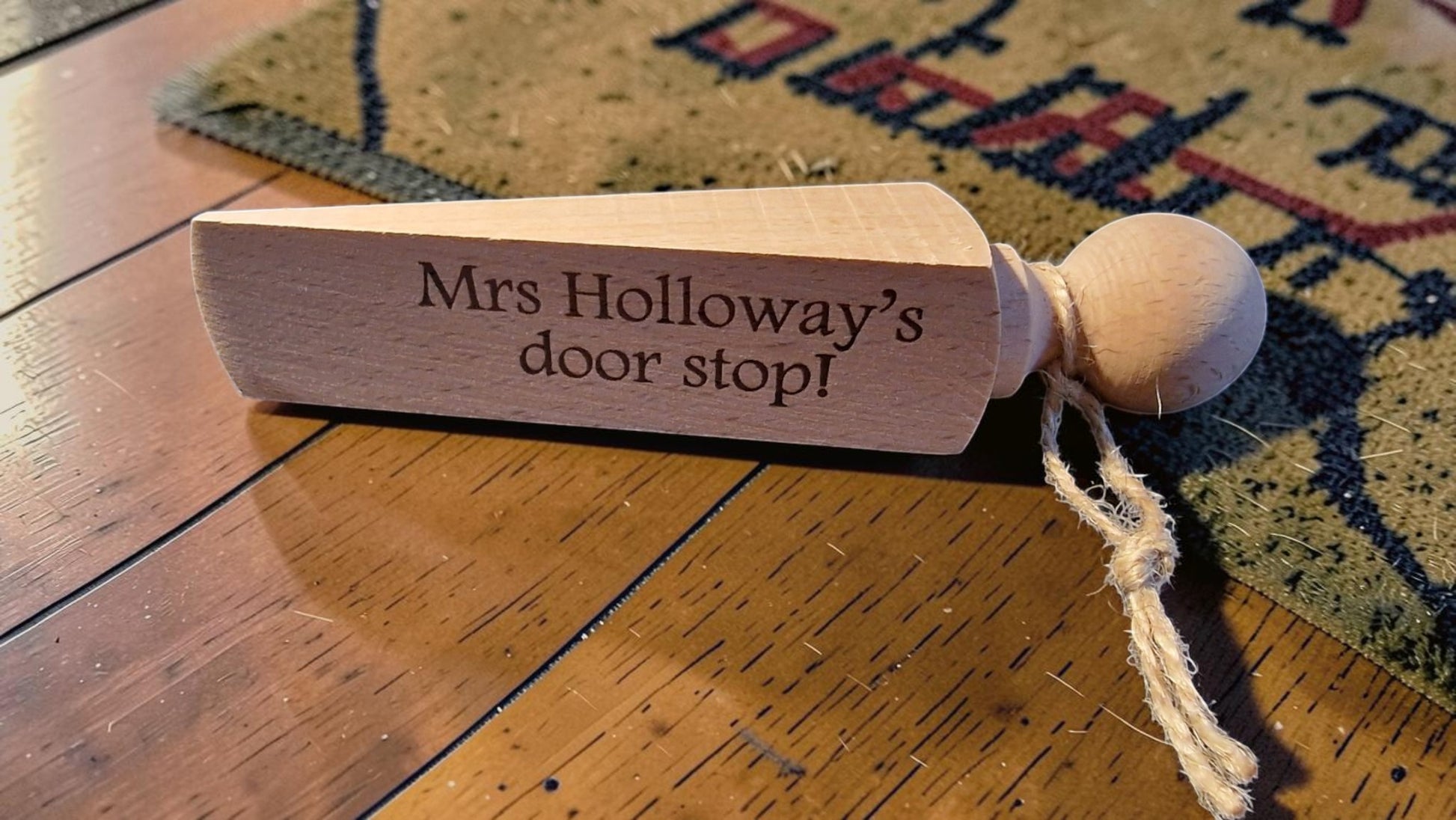 Wooden door stopper with 'Mrs Holloway's door stop!' engraving on a wooden floor.