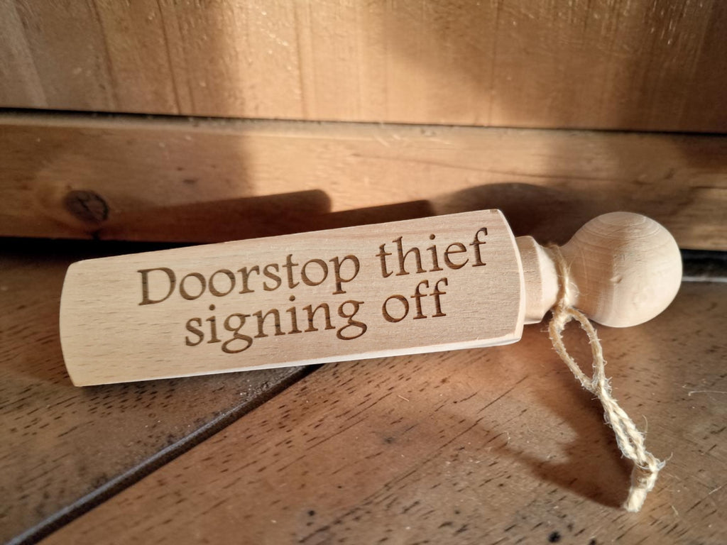 Wooden doorstop with 'Doorstop thief signing off' text on a wooden surface
