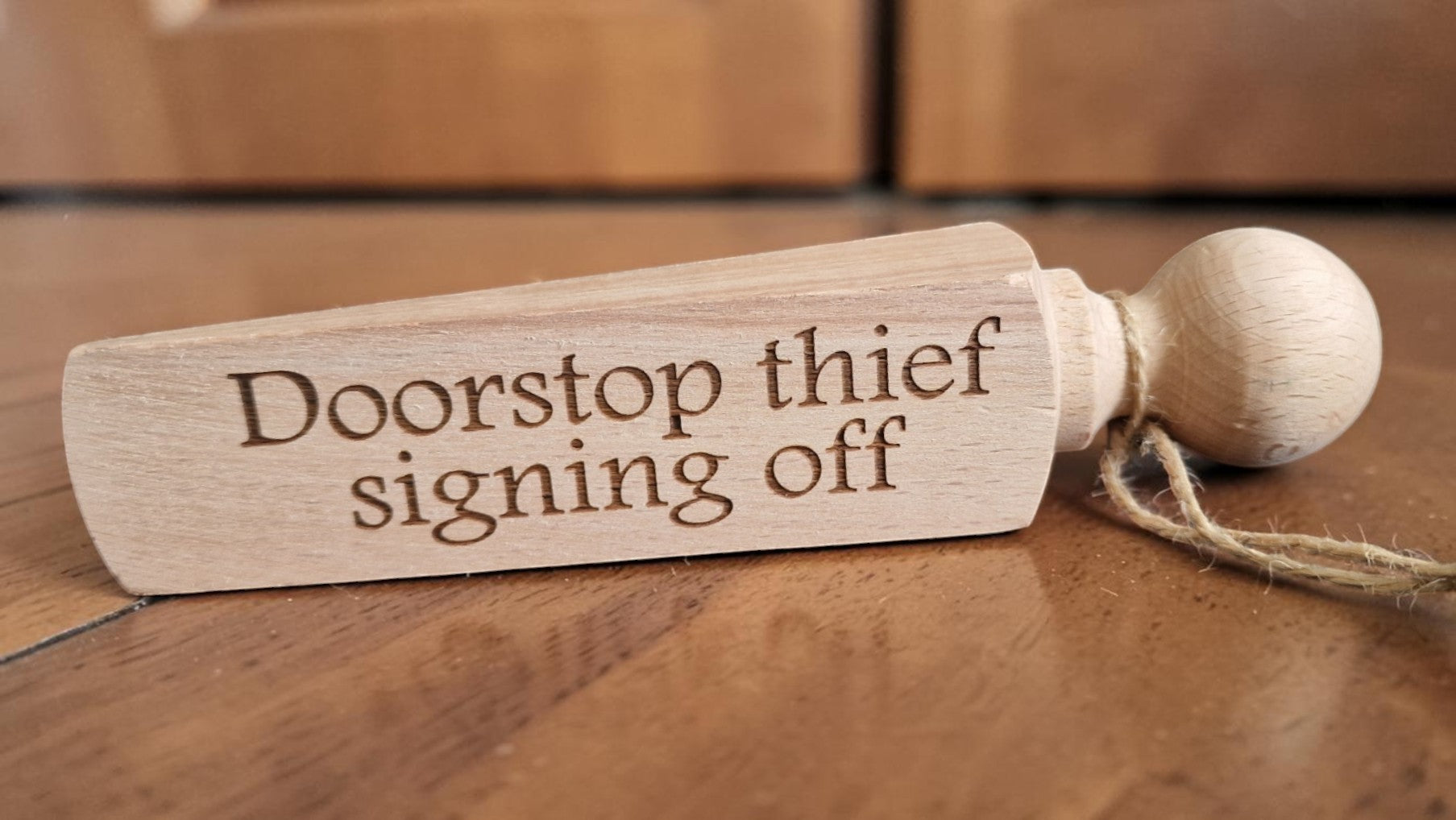 Wooden doorstop with 'Doorstop thief signing off' text on a wooden floor.