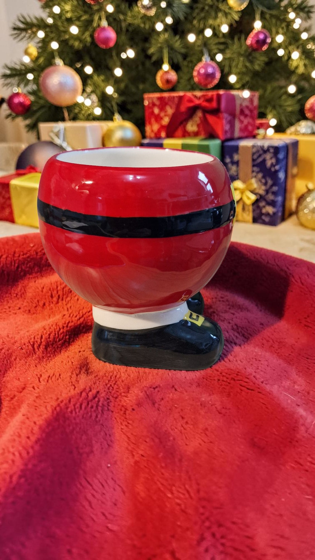 Red and black striped candy jar on a red surface with a Christmas tree and presents in the background.