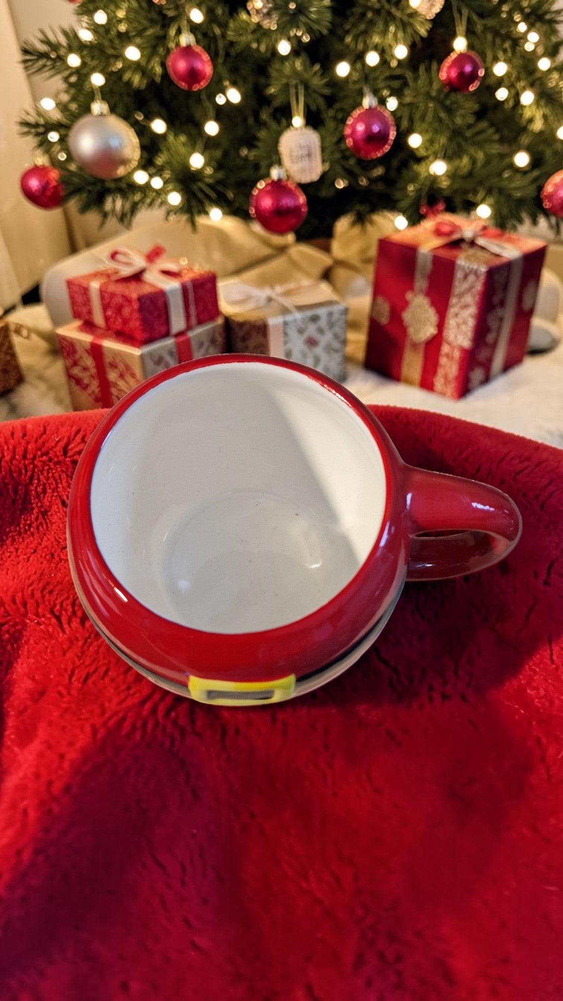 Red mug on a red surface with a Christmas tree and presents in the background