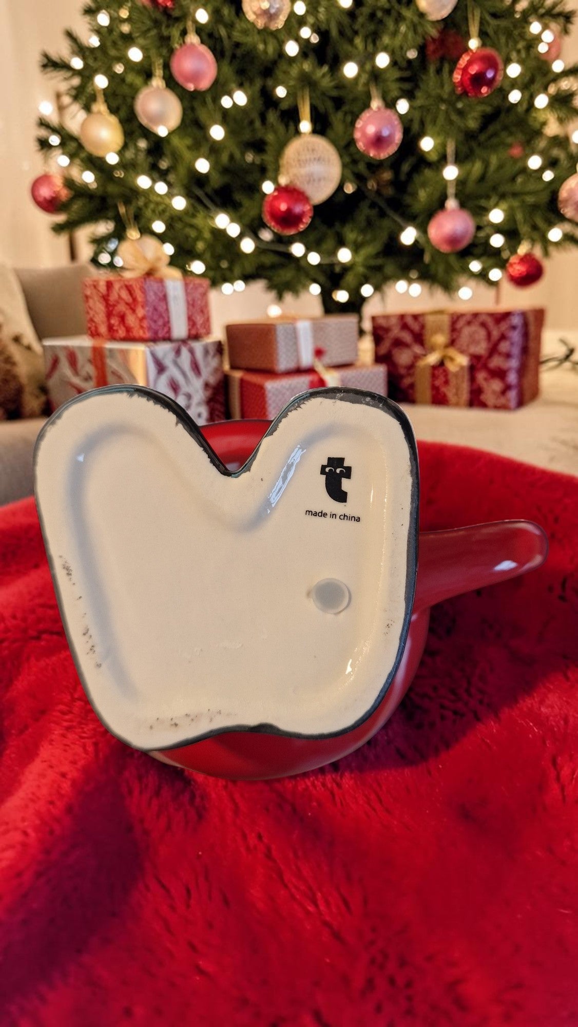 Heart-shaped white object with black logo on a red surface, Christmas tree and presents in the background