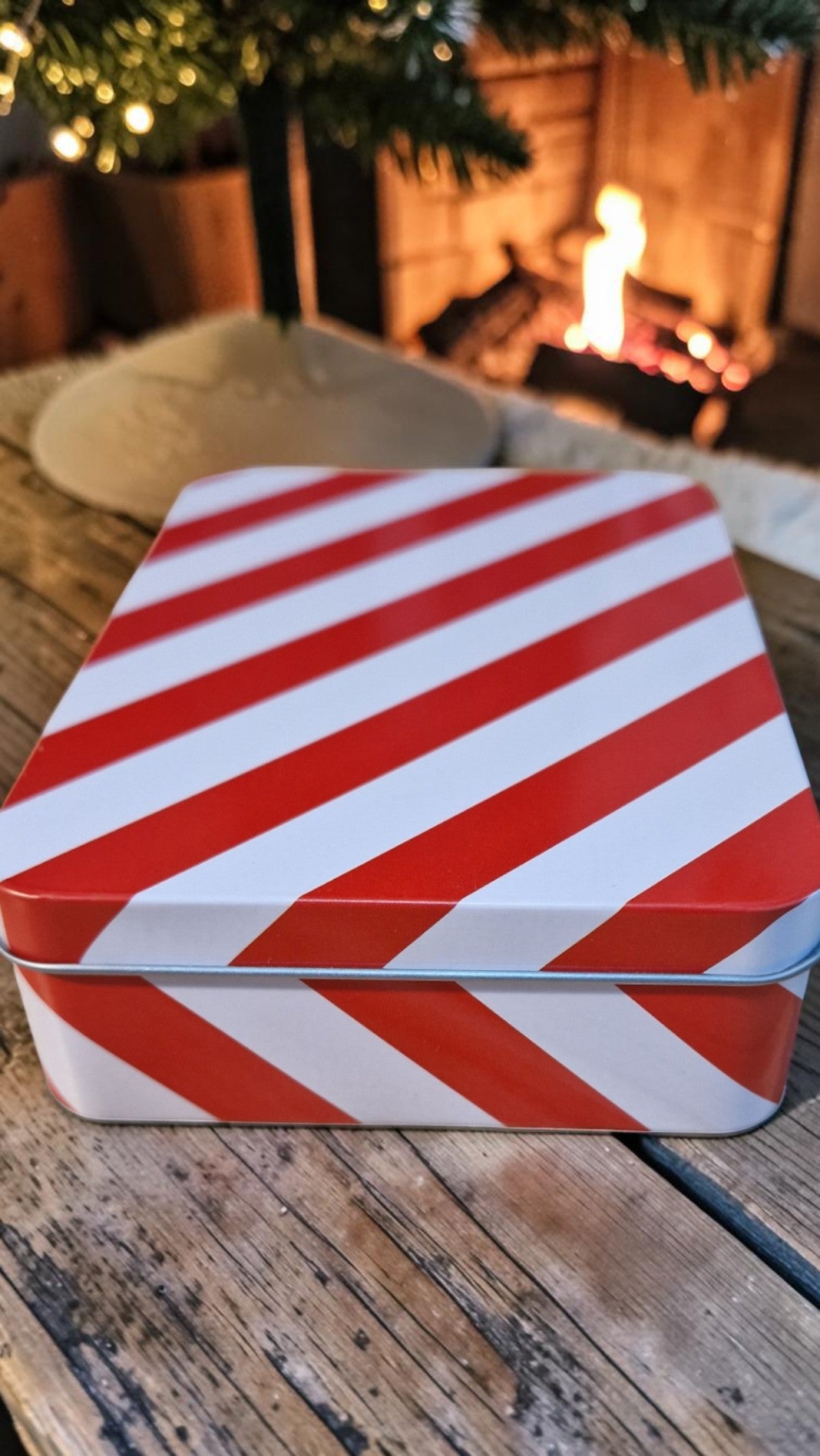 Red and white striped tin box on a wooden surface with a blurred festive background