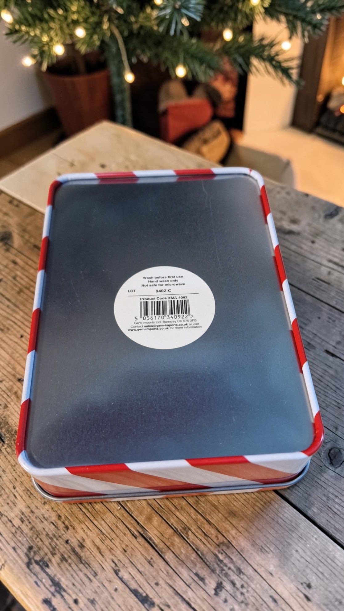 Tin box with a label on a wooden surface, Christmas tree in the background