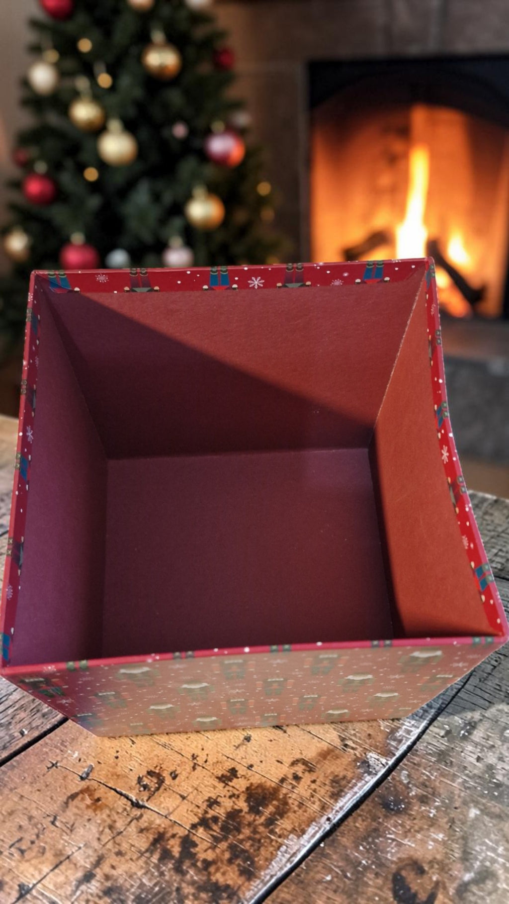 Red decorative box on a wooden surface with a Christmas tree and fireplace in the background