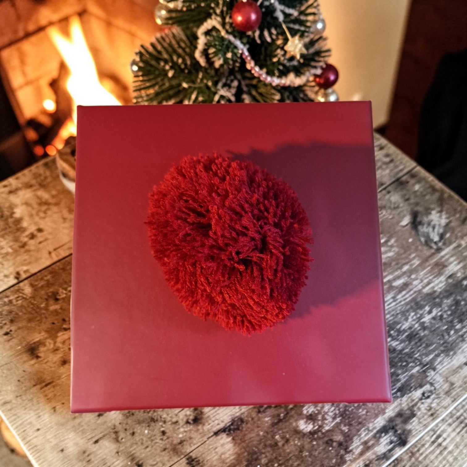 Red decorative ball on a red box with a Christmas tree and fireplace in the background