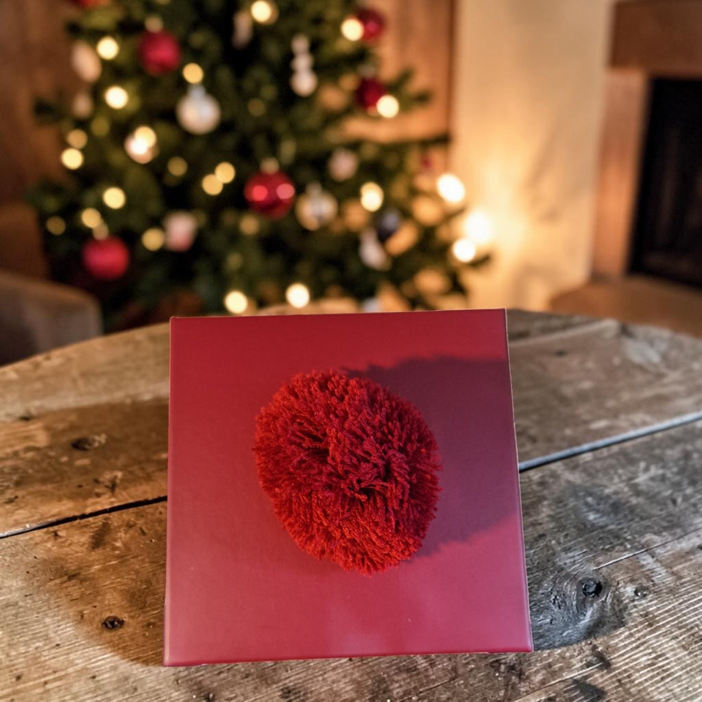 Red decorative item on a red card with a Christmas tree in the background