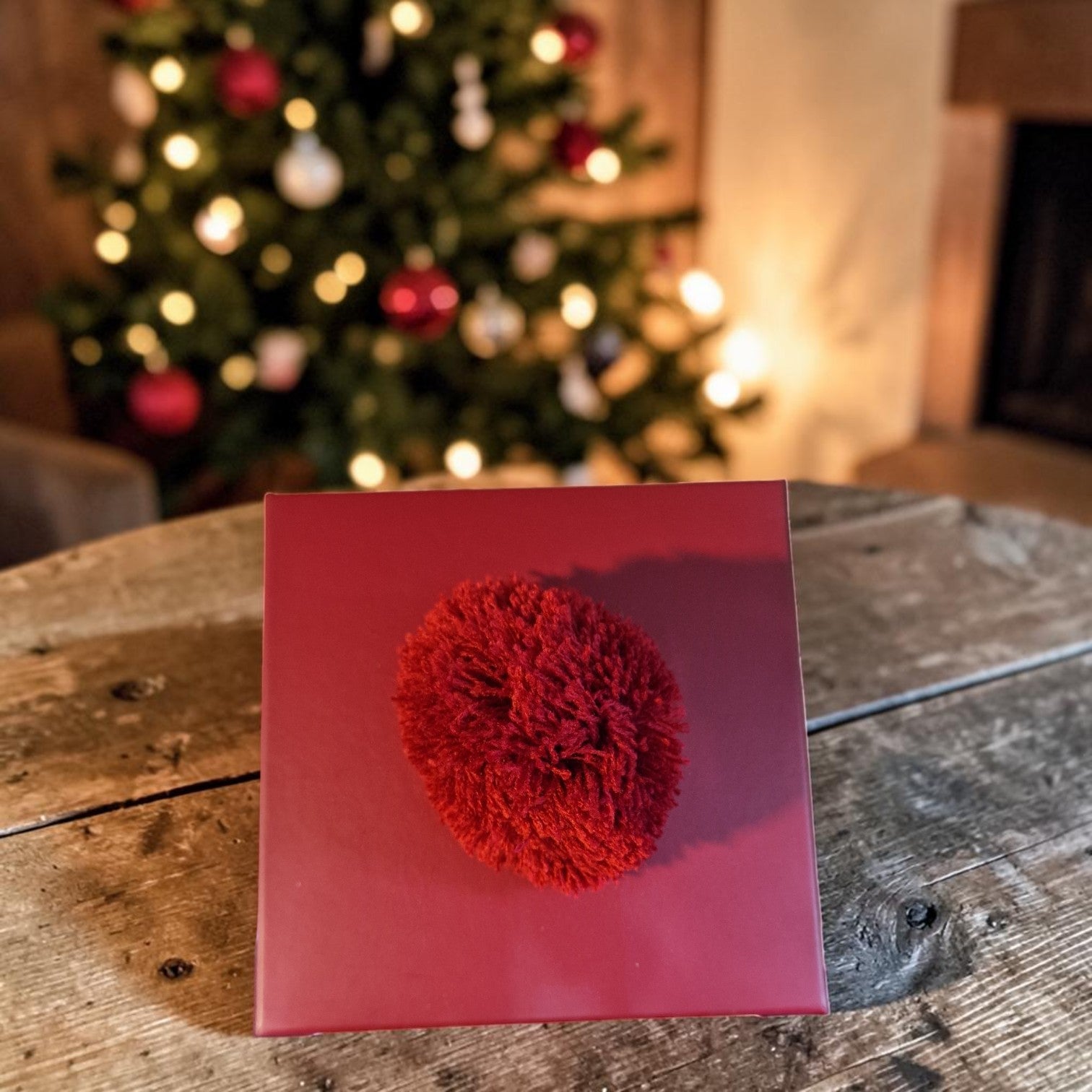 Red decorative item on a red card with a Christmas tree in the background