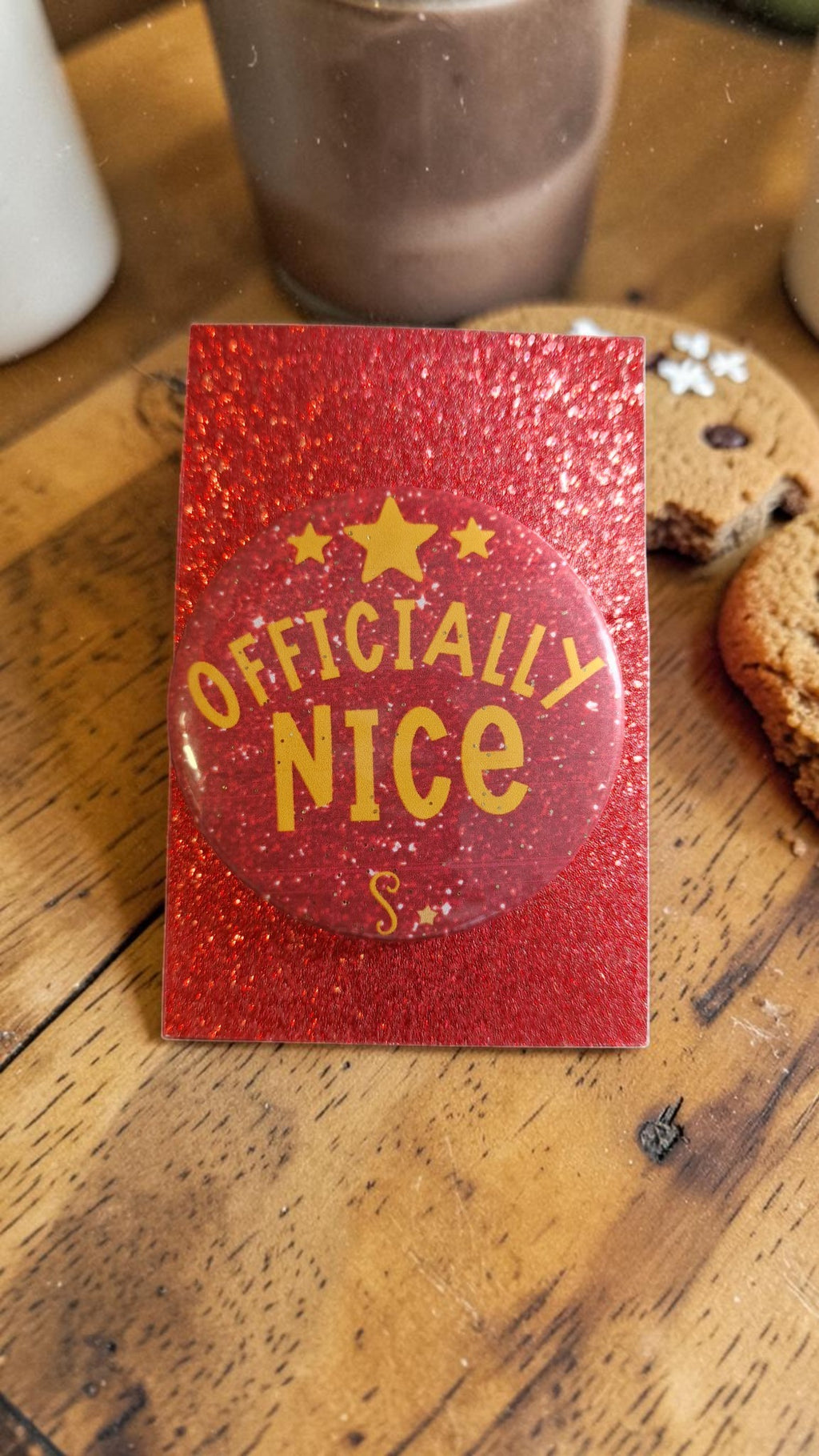 Red glittery card with 'Officially Nice' text on a wooden surface with cookies.