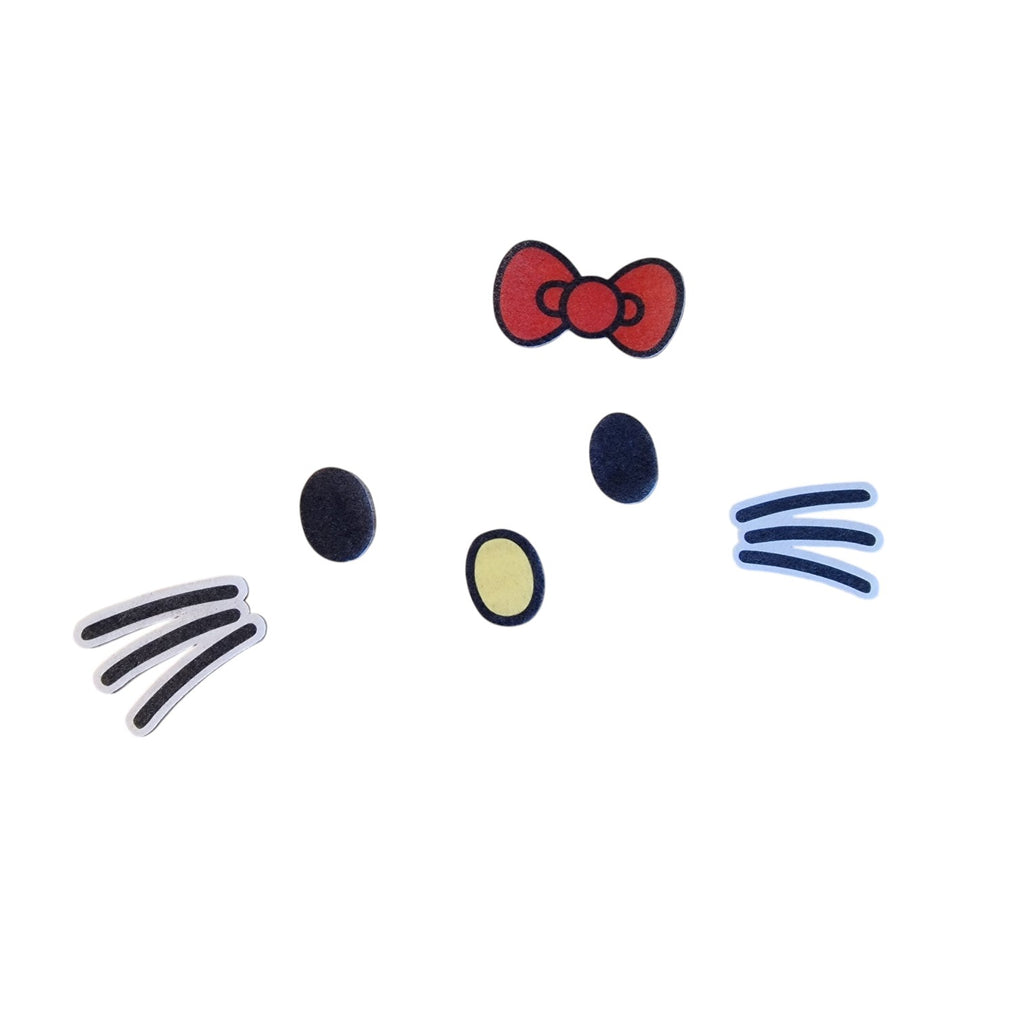 A flat lay of Hello Kitty face sticker pieces on a solid white background, including a red bow, black eyes, a yellow nose, whiskers, and ear details.