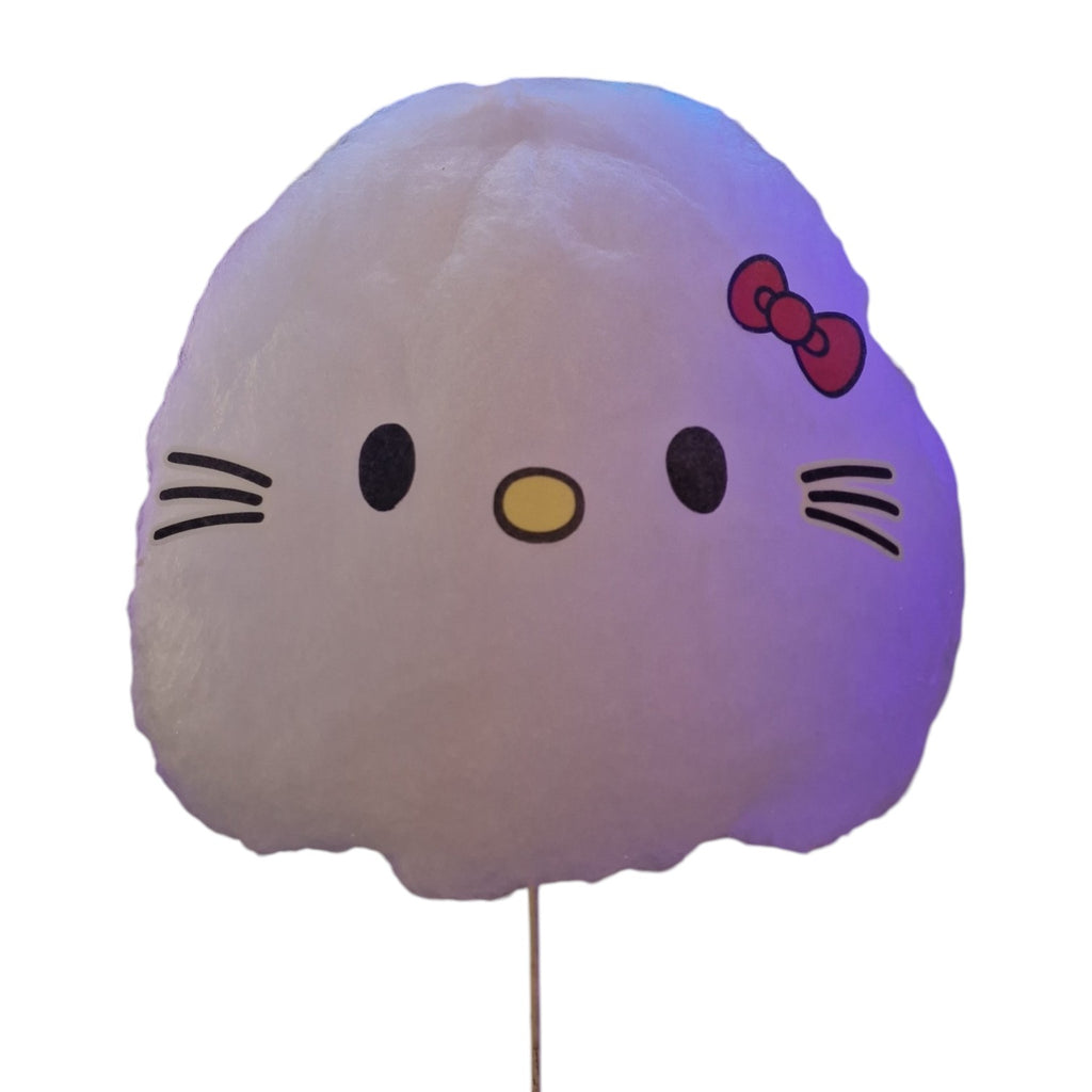 A Hello Kitty cotton candy plush toy on a stick, featuring the character's face with black whiskers, eyes, and nose, a red bow, and a soft white cotton candy body glowing with a purple hue.