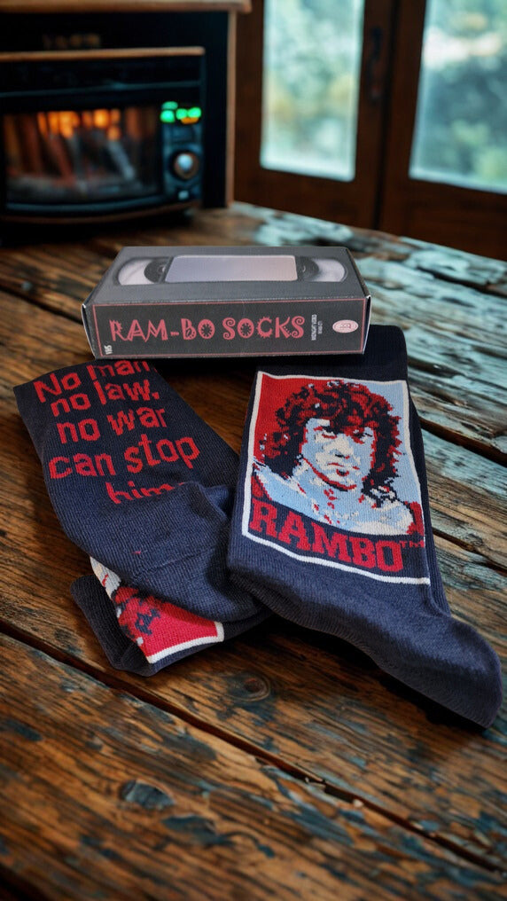 Two pairs of socks with 'Rambo' design on a wooden surface next to a VHS tape.