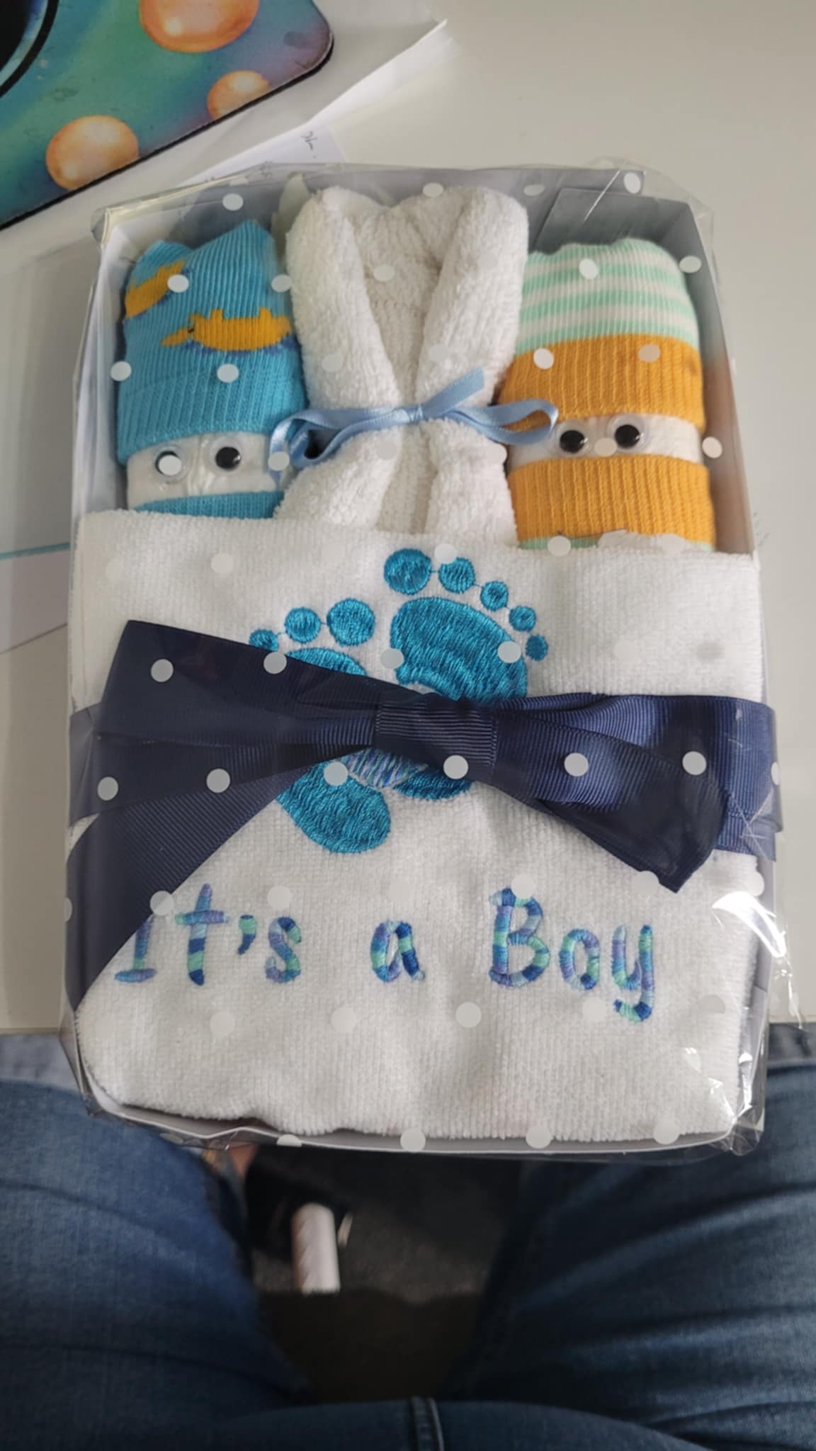 Baby shower gift set with socks and blanket labeled 'It's a Boy' on a lap.