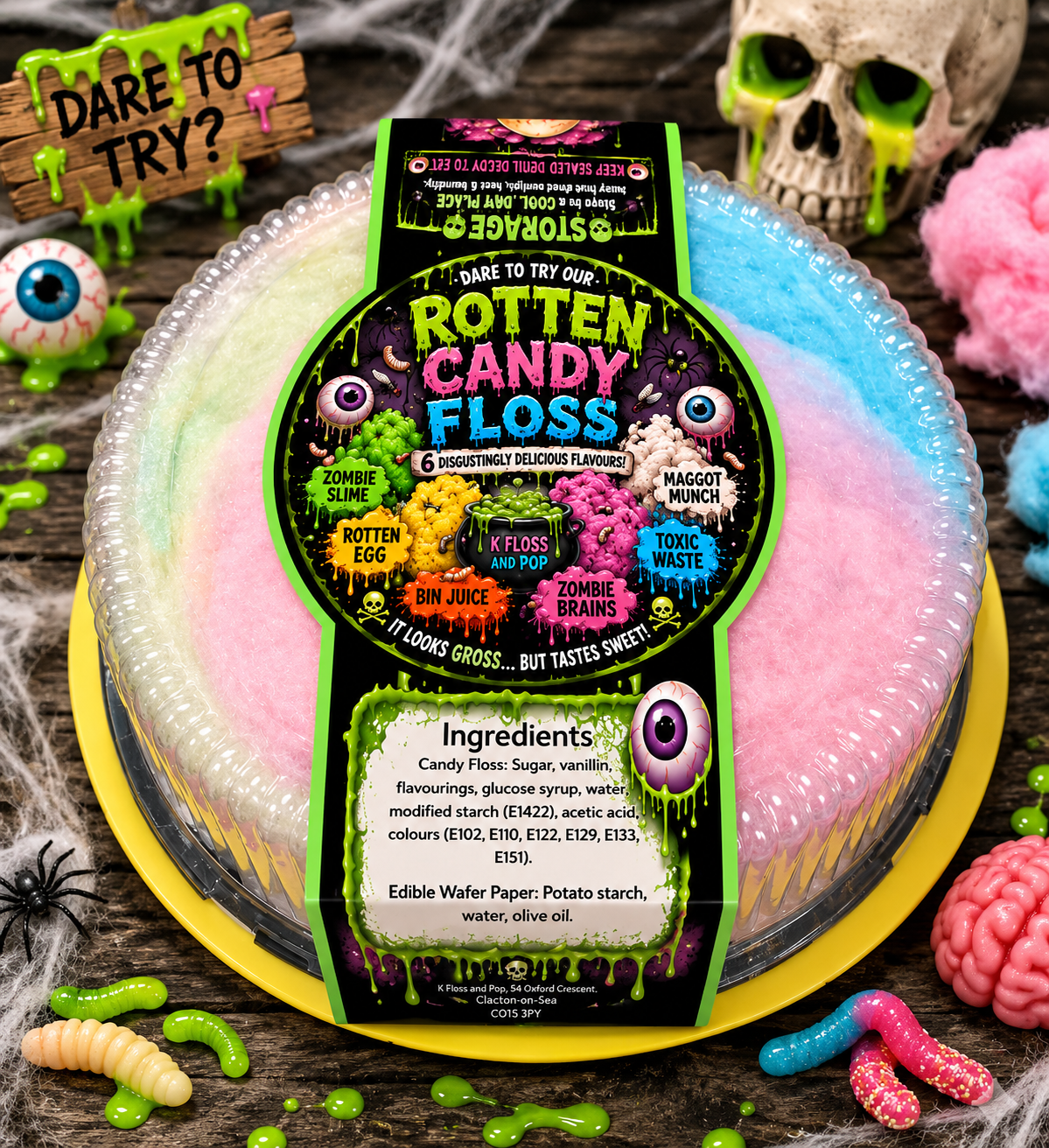 A novelty round cake styled to look like a pastel rainbow donut with a large 'Rotten Candy Floss' label on top, surrounded by Halloween props including fake worms, a skull, eyeballs, and a brain on a dark wooden surface.