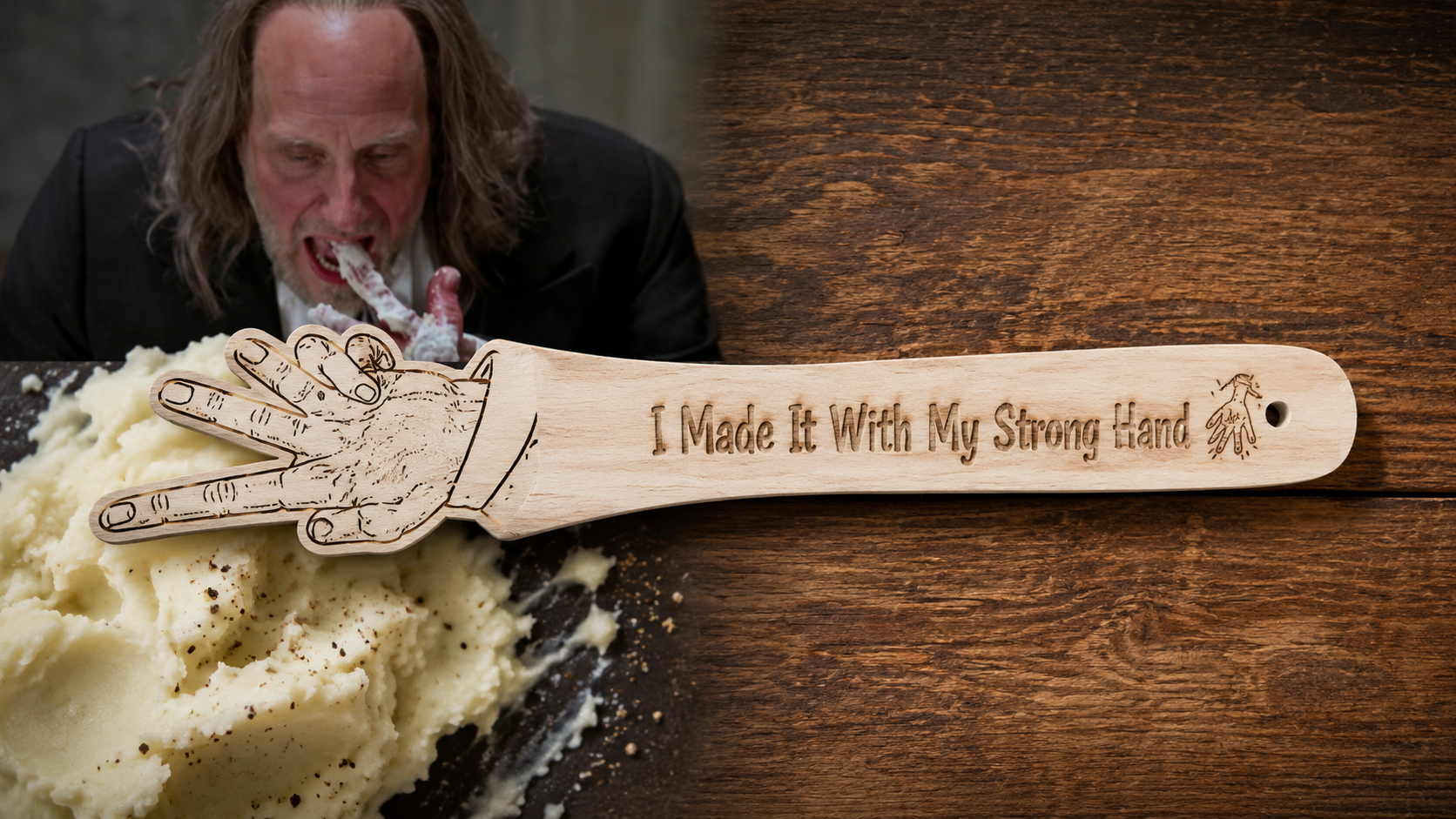 A wooden carving/spoon-shaped kitchen utensil engraved with 'I Made It With My Strong Hand' and a hand illustration, shown over mashed potatoes on a dark surface with a man in the background.