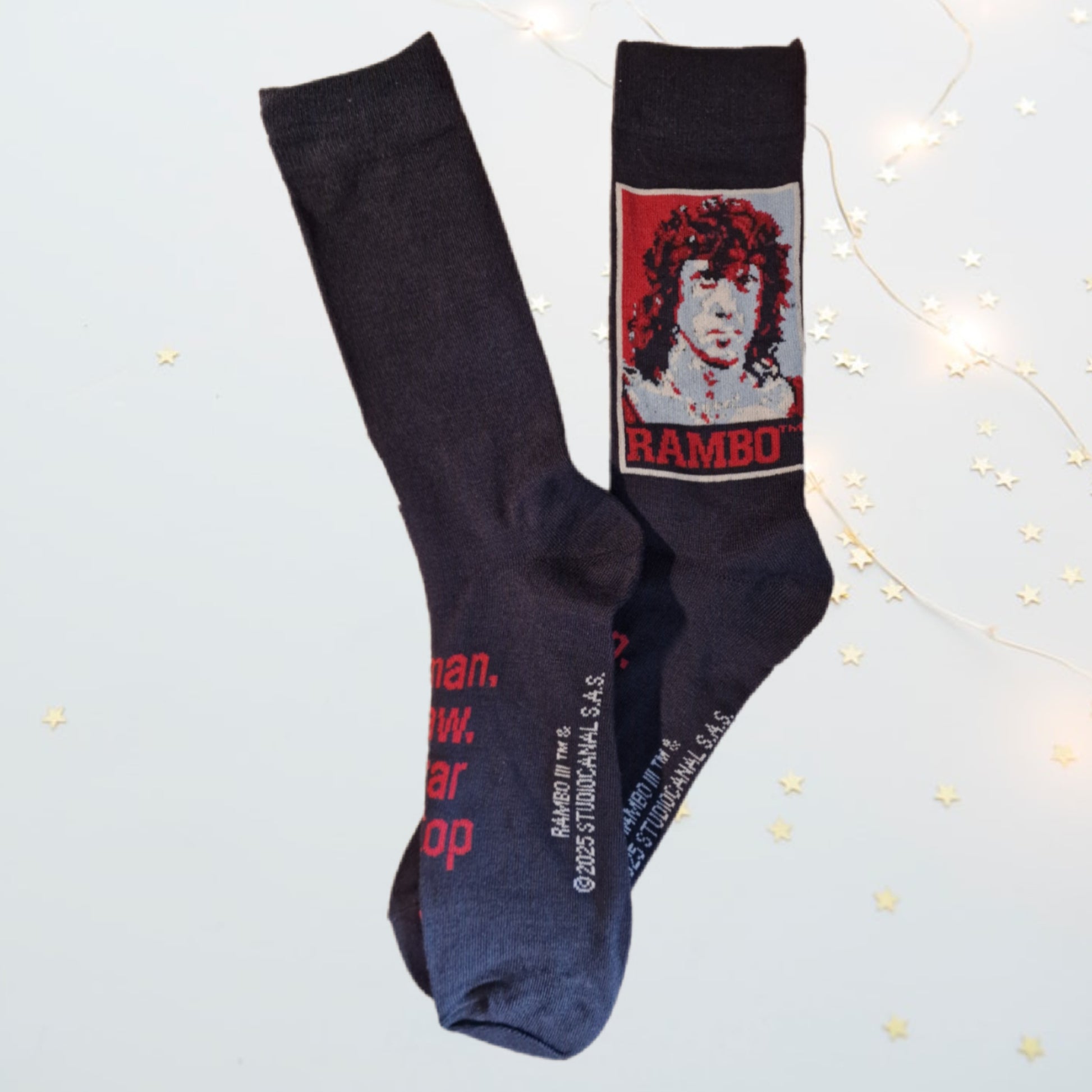 Black socks with a graphic of a person and the word 'RAMBO' on a light gray background.