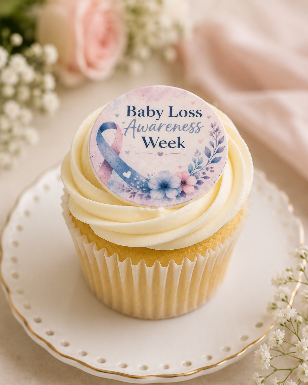 Cupcake with a 'Baby Loss Awareness Week' sticker on a decorative plate with flowers in the background