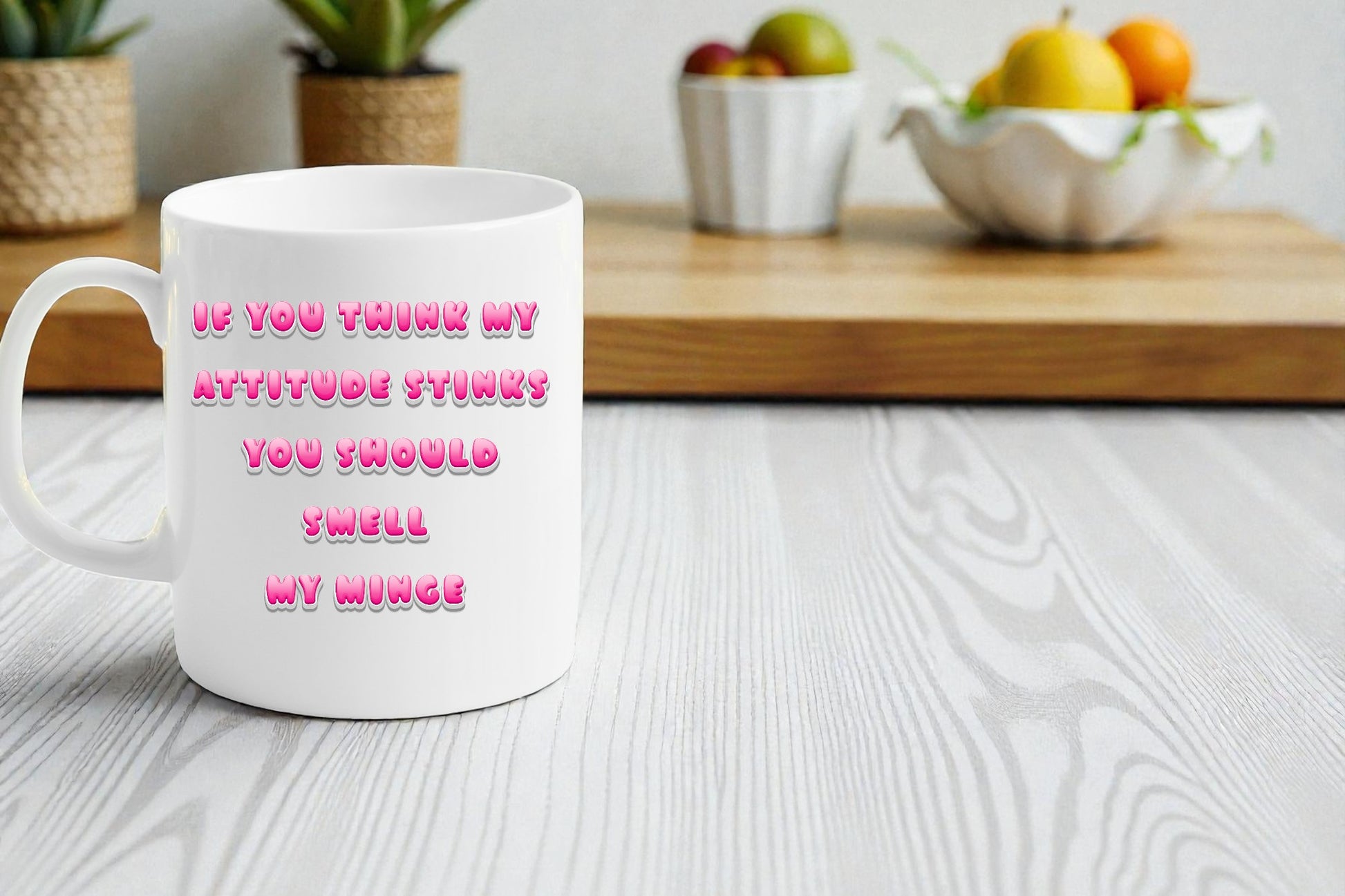 White mug with pink text on a white surface with a kitchen background