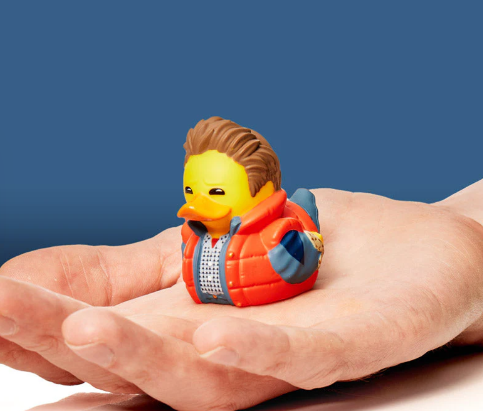 Toy duck wearing a jacket held in a hand against a blue background