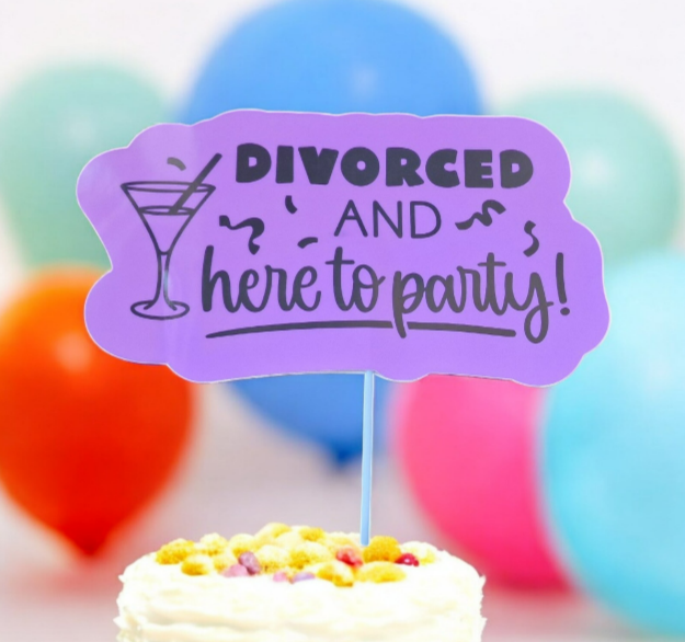 Purple cake topper reading “Divorced and here to party” with a cocktail glass illustration, displayed on a cake with colourful balloons in the background