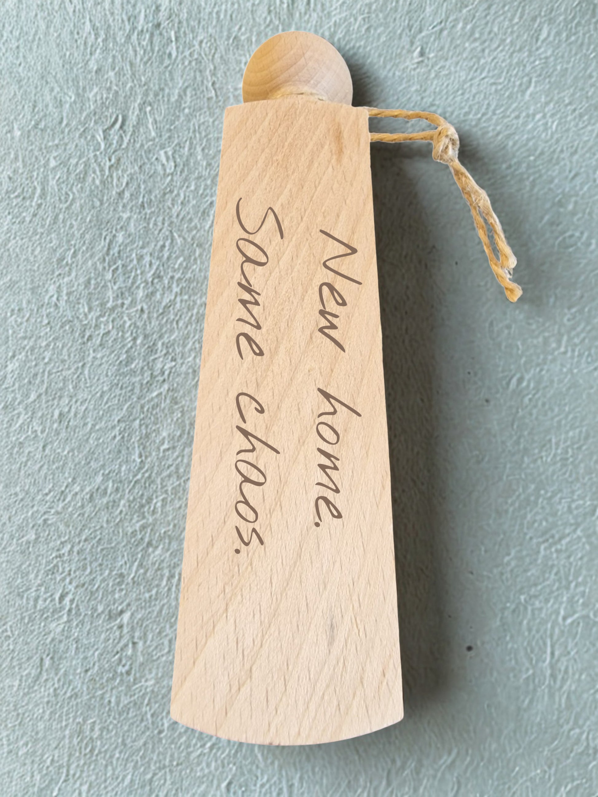 Wooden object with 'New home, same chaos' engraving on a light blue background