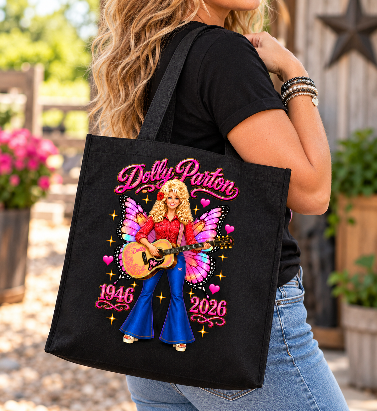 A woman outdoors carrying a black canvas tote bag with a colorful Dolly Parton graphic. The bag features pink script text reading 'Dolly Parton,' an illustration of Dolly with pink wings playing a guitar, and the years '1946' and '2026.