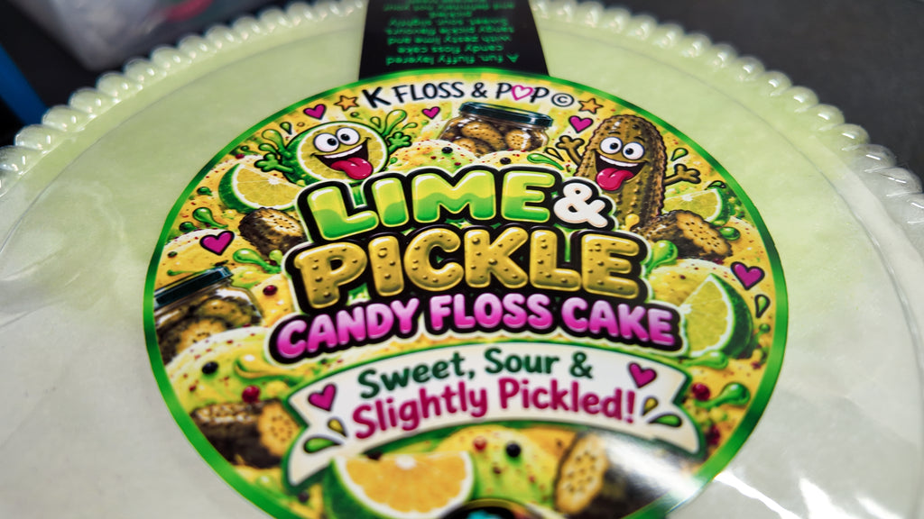 A close-up of a round product label for K Floss & Pop Lime & Pickle Candy Floss Cake, featuring bright lime green, yellow, pink, and white graphics with candy floss characters and citrus imagery.