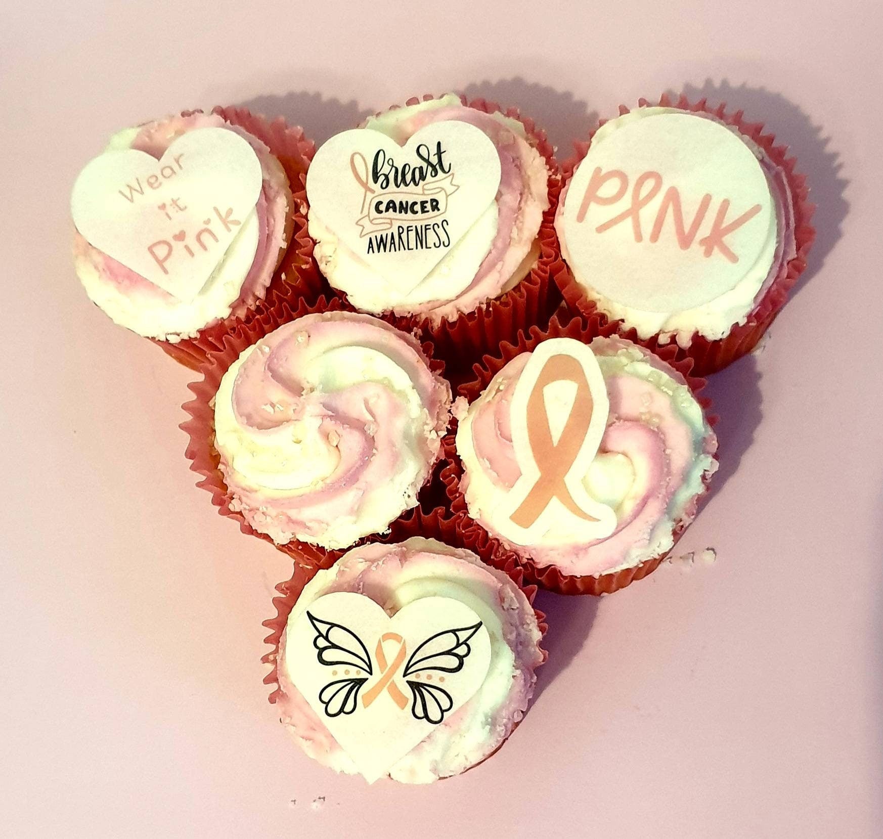 Assorted breast cancer awareness edible pre cut cake toppers featuring pink ribbons, hearts, butterflies, and supportive messages, arranged neatly on a light wood background.