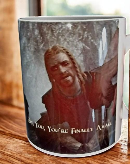 Black color change mug with “Hey you’re finally awake” Ralof design revealed by heat, shown as a fun gamer and coffee lover gift.