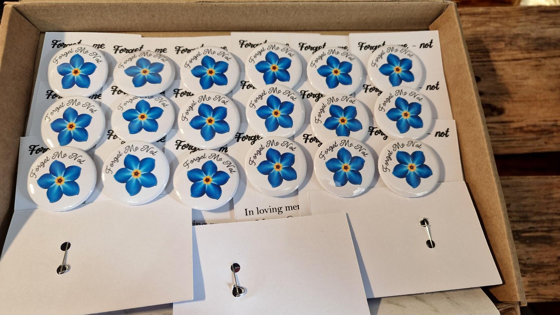 Set of 20 forget me not funeral badges on personalised “In Loving Memory” cards, displayed as keepsake mementos for funerals or dementia remembrance.
