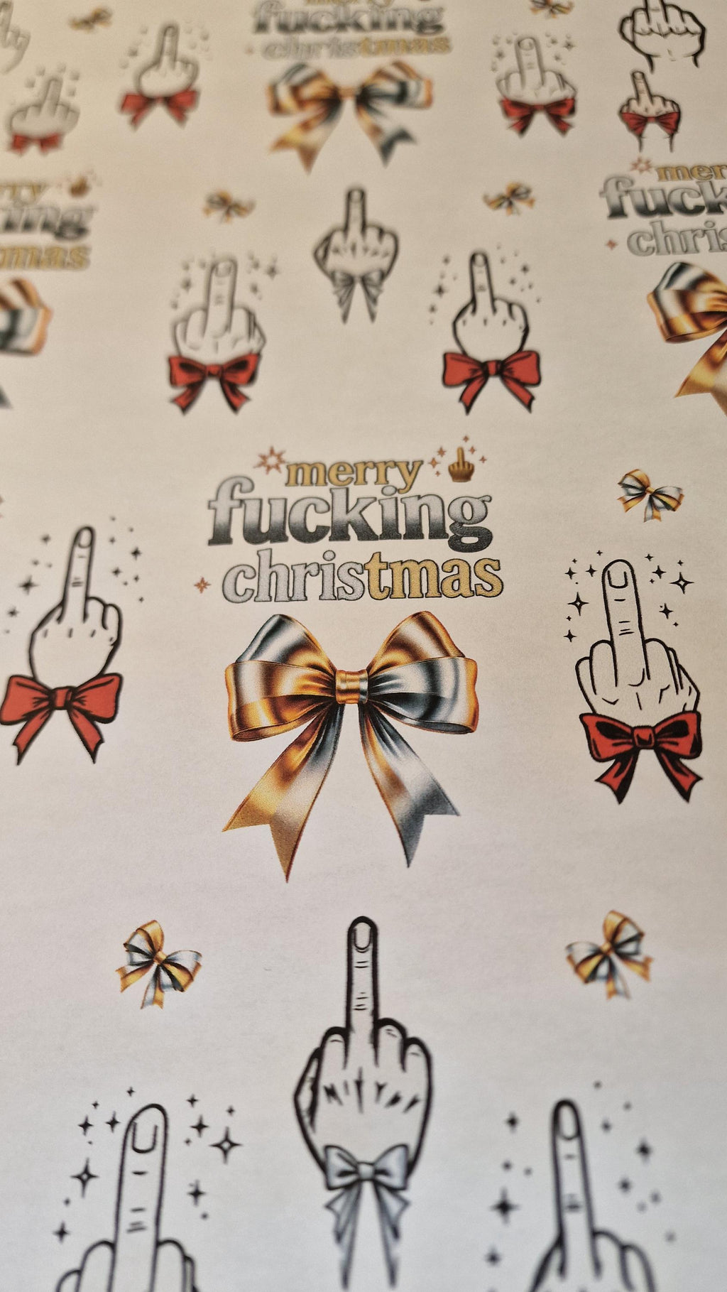 Two sheets of Merry Fucking Christmas wrapping paper with a cheeky middle finger design, displayed as funny Secret Santa gift wrap.