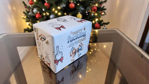 Two sheets of Merry Fucking Christmas wrapping paper with a cheeky middle finger design, displayed as funny Secret Santa gift wrap.