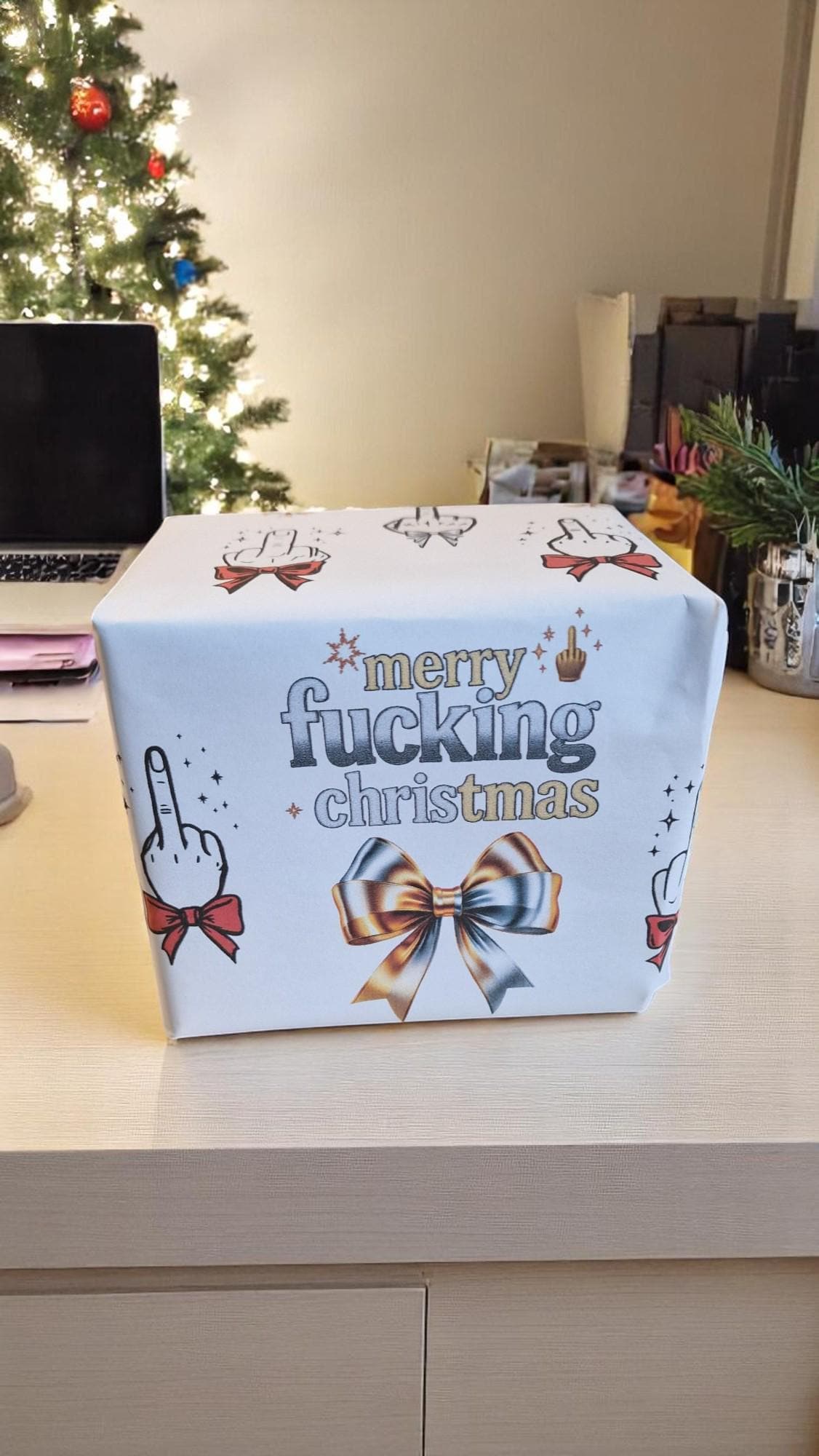 Two sheets of Merry Fucking Christmas wrapping paper with a cheeky middle finger design, displayed as funny Secret Santa gift wrap.