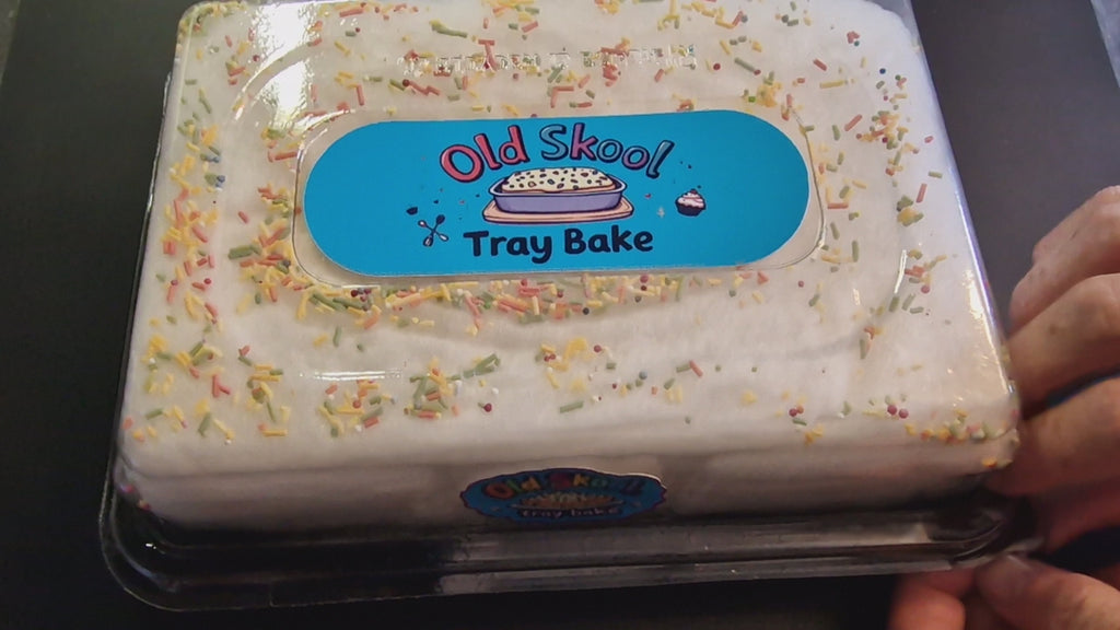 Old Skool traybake candyfloss cake in a shareable tray package, showing layers of fluffy cookies and cream, cream cheese, and raspberry floss, topped with colourful 100s and 1000s sugar strands, set on a picnic blanket with mugs and lemonade.