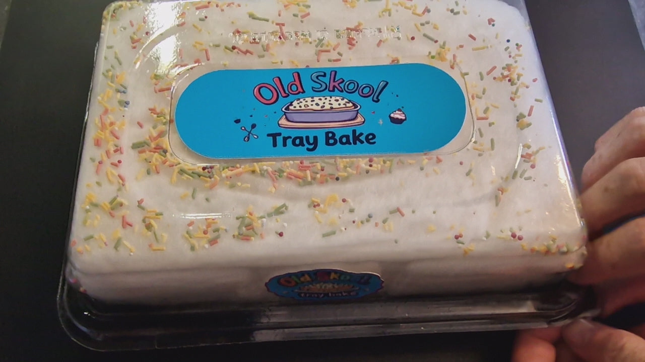 Old Skool traybake candyfloss cake in a shareable tray package, showing layers of fluffy cookies and cream, cream cheese, and raspberry floss, topped with colourful 100s and 1000s sugar strands, set on a picnic blanket with mugs and lemonade.
