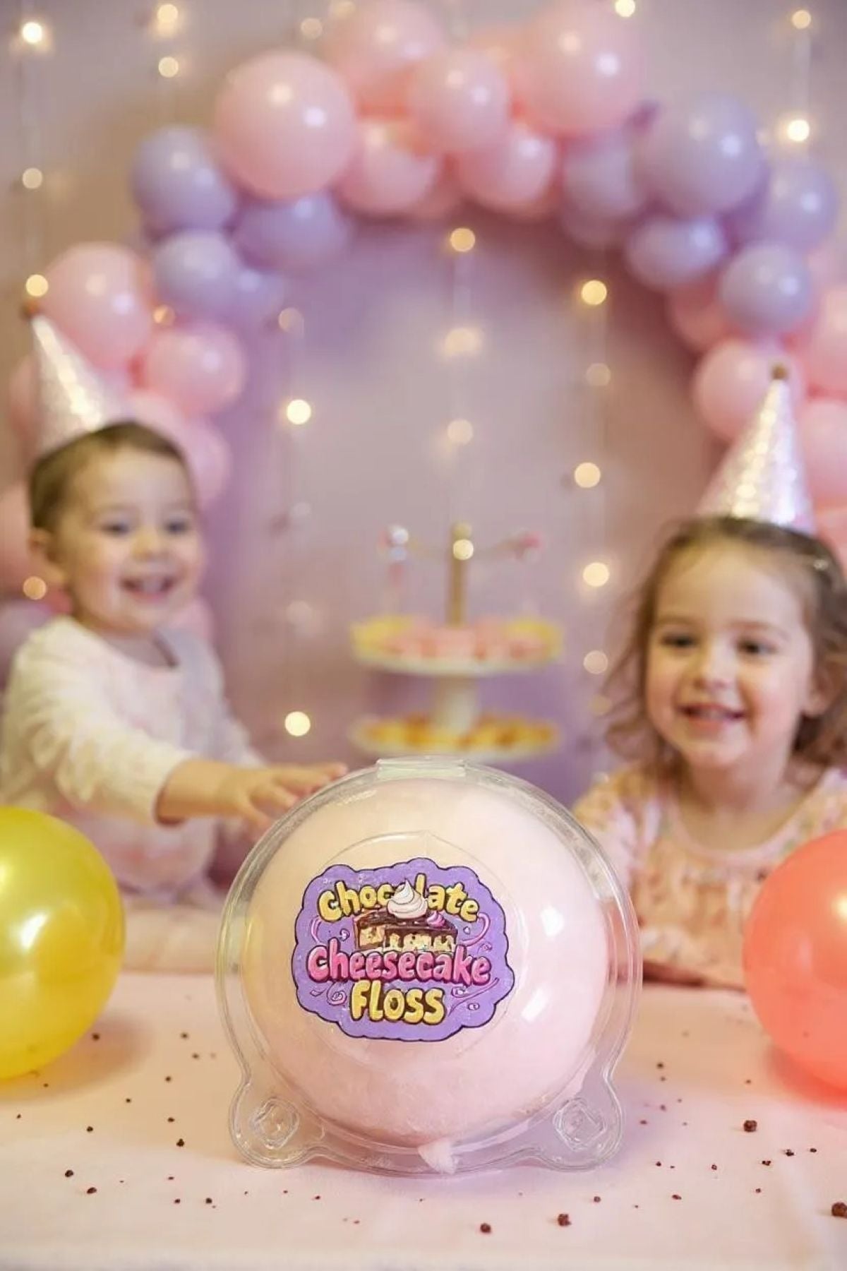 Children at a birthday party with balloons and a container of chocolate cheesecake floss.
