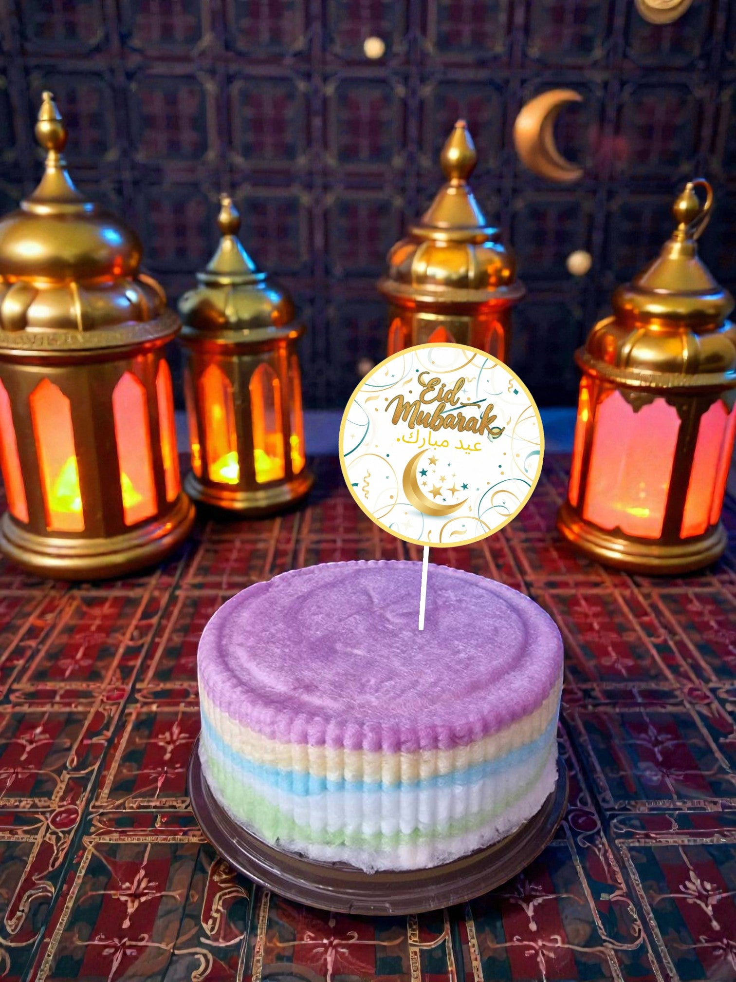 Decorative cake with a 'Eid Mubarak' topper in front of lit lanterns on a patterned background