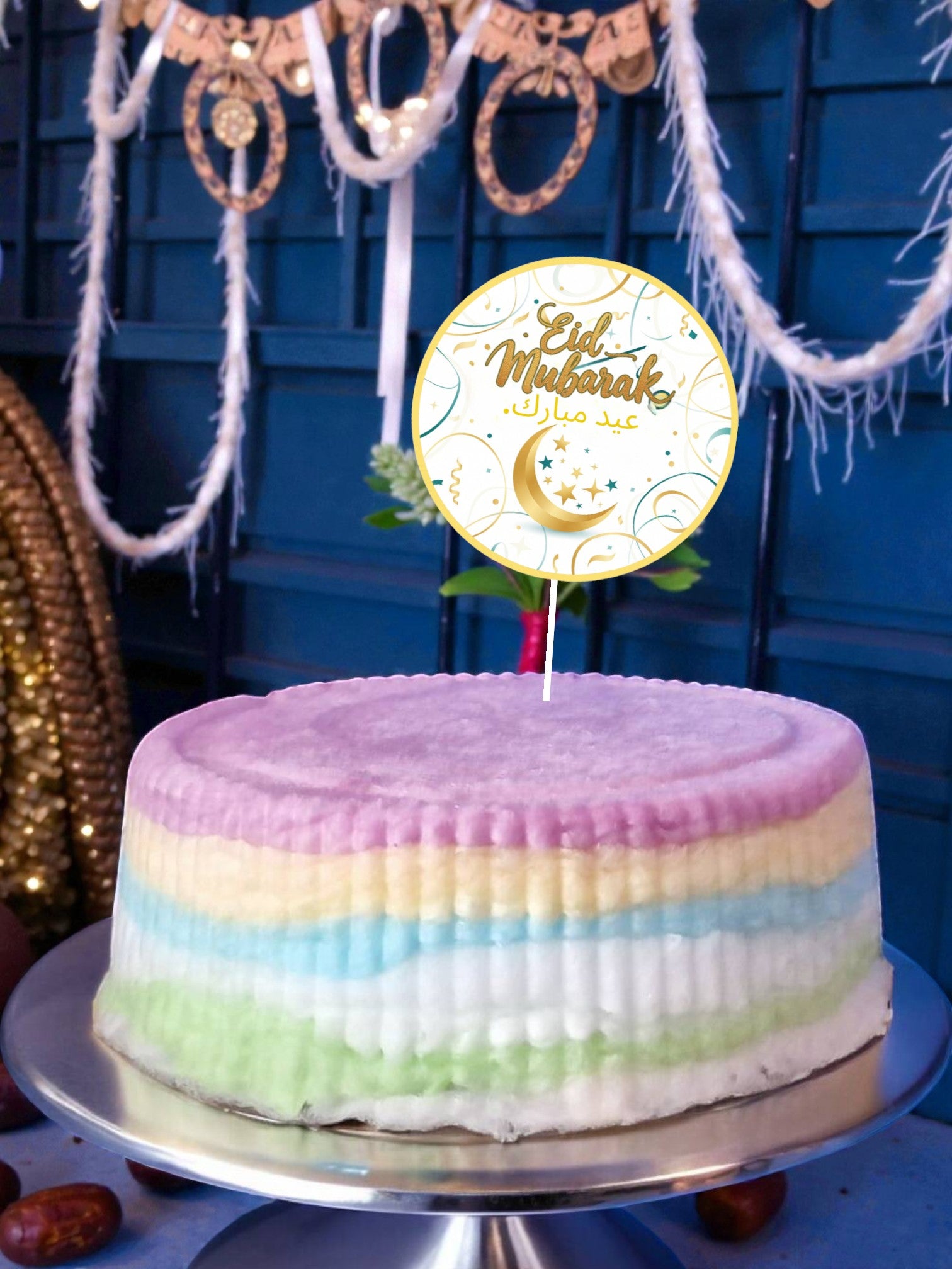Colorful cake with an 'Ed Mubarak' topper against a blue wall with decorations.