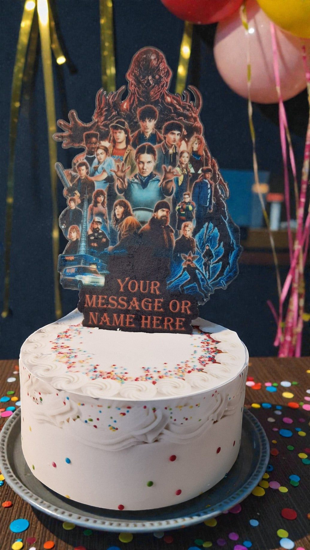White cake with a decorative topper featuring a collage of people and the text 'Your Message or Name Here' against a dark background with balloons.