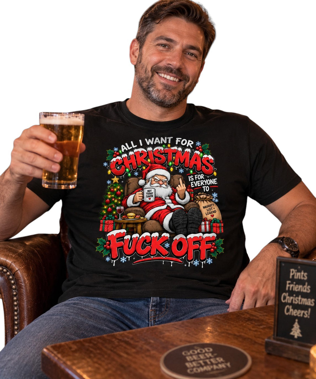 A man sitting in a brown leather armchair holds a glass of beer and wears a black graphic t-shirt featuring a festive Christmas design with Santa Claus and the text 'ALL I WANT FOR CHRISTMAS IS FOR EVERYONE TO FUCK OFF'.